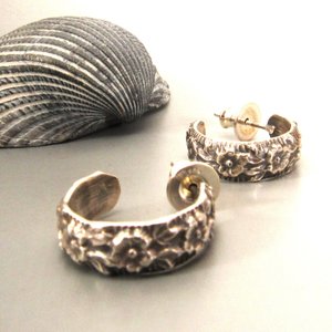 A pair of small silver stud hoop earrings with a floral design. The earrings are made of sterling silver and have a polished finish.