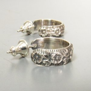 A pair of sterling silver post back hoop earrings with a floral design. The earrings have a polished finish.