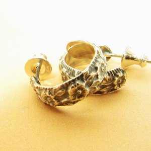 Silver hoop earrings with a floral design. The earrings have a floral textured  pattern. Photo on orange  bacground