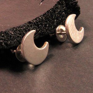 A pair of silver crescent moon stud earrings. The earrings are made of sterling silver and have a simple, modern design.