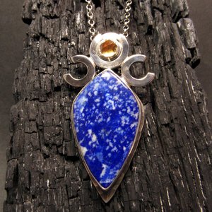 Triple goddess / moon pendant necklace with a faceted citrine and large lapis lazuli cabochon crafted from argentium sterling silver, fine silver. Pendant measures 2 inches from the top and is 7/8 inch across widest part and is suspended on a 18 inch sterling silver chain. Displayed against charred wood.