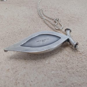Reverse side showing makers mark .935 argentium purity.Soft elegance meets artisan craftsmanship in this one of a kind handcrafted pendant featuring a beautifully pastel pink opal set in textured Argentium® sterling silver. The unique, petal-shaped stone in a petal shaped setting radiates gentle warmth in a soothing blush hue—perfect for those who adore subtle statement pieces with soulful charm. 2.25" long x 7/8" wide.
