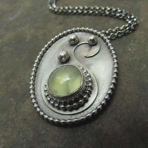 Argentium sterling silver and luminous green prehnite paisley necklace on dark stone colored background, with rolo chain partially visible.
