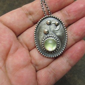 Green prehnite stone cabochon and sterling silver pendant necklace photographed in hand.