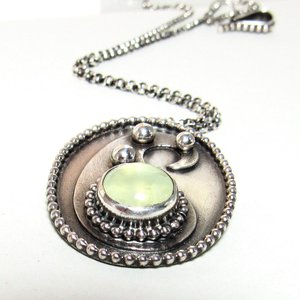 Argentium sterling silver, and prehnite cabochon paisley necklace on white background, lying flat. Sterling silver rolo chain and clasp trailing in the background.