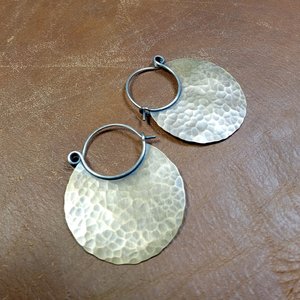 Large hammered mixed metal hoop earrings on leather background.