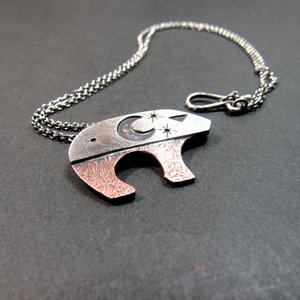 Celestial bear pendant inspired by the Ursa Major constellation, combining polished sterling silver and warm oxidized copper, featuring moon and star details that allow the copper to peek through the silver.  18 inch SS cain and findings complete the bear pendant necklace. Displayed on grey background.