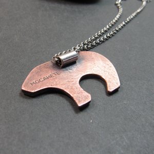 Reverse side of mixed metal bear pendant showing bail and makers mark "Mocahete" The necklace is displayed against a dark background.