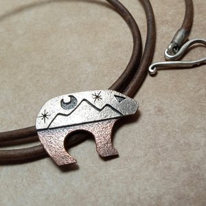 Close up of mixed metal bear pendant on leather cord.