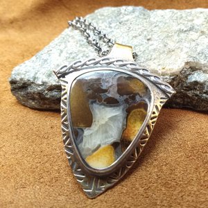 Cobra jasper, bronze and sterling silver pendant by Mocahete, photographed against a rock on leather.