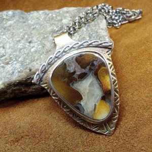 Cobra jasper pendant showing swirls of earthy colors in its matrix. SS chain and handmade findings. Photo against rock on leather.