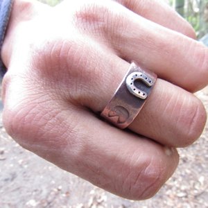 Wide rustically textured copper band with silver horseshoe and horse hoof print stamp motif. Ring has been oxidized and polished giving it a deep and rich patina, and is photographed on the makers hand with the horseshoe facing forward. Band is made in whole and half sizes from 6-16.