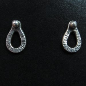 Sterling silver post back or stud earrings shaped like a raindrop and textured. A small orb of silver at the top is the crowning touch. Earrings measure 1/2" long and 1/4" wide. Comes with SS backs not pictured here.Displayed on black background with earrings facing forward.