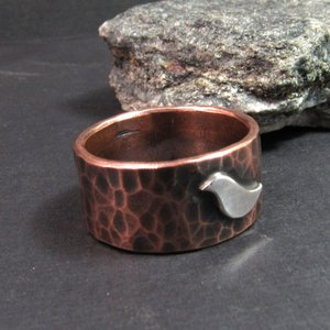 Rustic copper ring with silver bird, wide band perfect for men, women, unisex. Photo against rock on dark background.