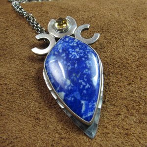 Triple goddess / moon pendant necklace with a faceted citrine and large lapis lazuli cabochon crafted from argentium sterling silver, fine silver. Pendant measures 2 inches from the top and is 7/8 inch across widest part and is suspended on a 18 inch sterling silver chain. Displayed against brown leather.