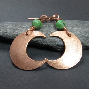 Up close photo of handmade copper crescent moon dangle earrings with faceted green chrysoprase beads. Earrings measure 2 and 1/8" long and the moon is 3/8" wide at widest point.The ear wires are solid, pure copper. Displayed against black rock on dark background.