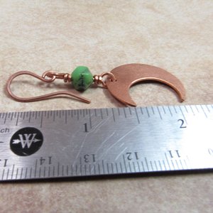 Handmade copper crescent moon dangle earrings with faceted green chrysoprase beads. Earrings measure 2 and 1/8" long and the moon is 3/8" wide at widest point.The ear wires are solid, pure copper. Displayed against ruler on neutral background.