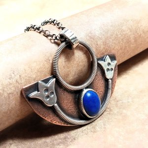 Side view of handcrafted mixed metal lotus pendant in argentium silver and copper with lapis lazuli cabochon. Displayed on neutral background.