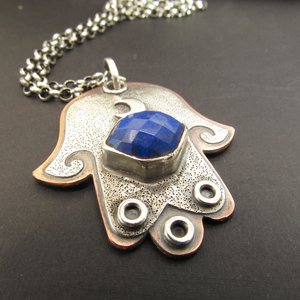 Mixed metal, copper and argentium sterling silver hamsa pendant necklace with lapis lazuli cabochon and crescent moon detail. 19 inch ss chain and findings. Hamsa is 1.5" wide x 1.75" tall. Displayed on dark grey background, pendant is facing forward.