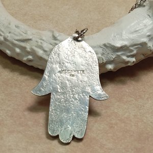 Reverse side of Hamsa pendant necklace showing makers mark and argentium purity. Displayed against antler on neutral background.