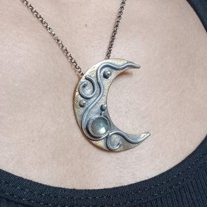 Crescent moon pendant in bronze and silver with labradorite cabochon. Shown being worn on a person with black tank top.