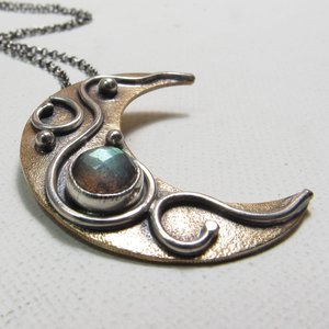 Mixed metal, bronze and argentium SS moon pendant with faceted labradorite cab. Displayed on white background.