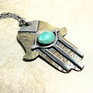 Bronze and silver hamsa pendant necklace with green stone displayed on neutral background. Pendant measures 1.5" wide x 2" long.