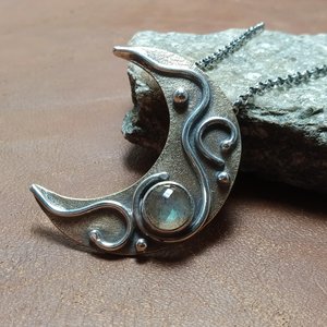Labradorite mixed metal pendant necklace displayed against rock on beige background.