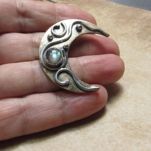 Moon pendant in bronze and silver with labradorite photo in hand on neutral background.