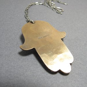 Reverse side of bronze and silver hamsa showing makers mark " Mocahete". Displayed on grey background.