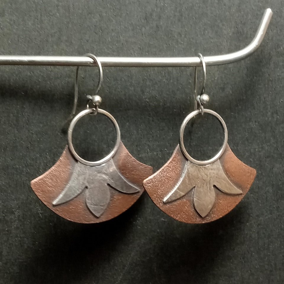 Swingy fan shape earrings in mixed metals with floral detail. Displayed hanging from stand.