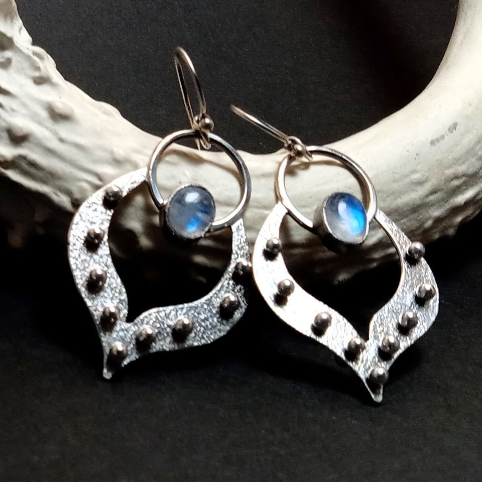 Tribal influenced Argentium silver lotus petal earrings with moonstones. Displayed against white antler on black background.