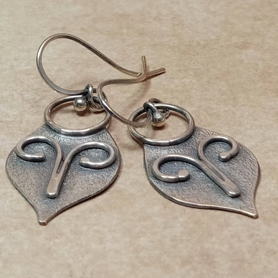 Argentium silver dangle earrings in a mask shape with wire embellishment. Displayed on neutral background.