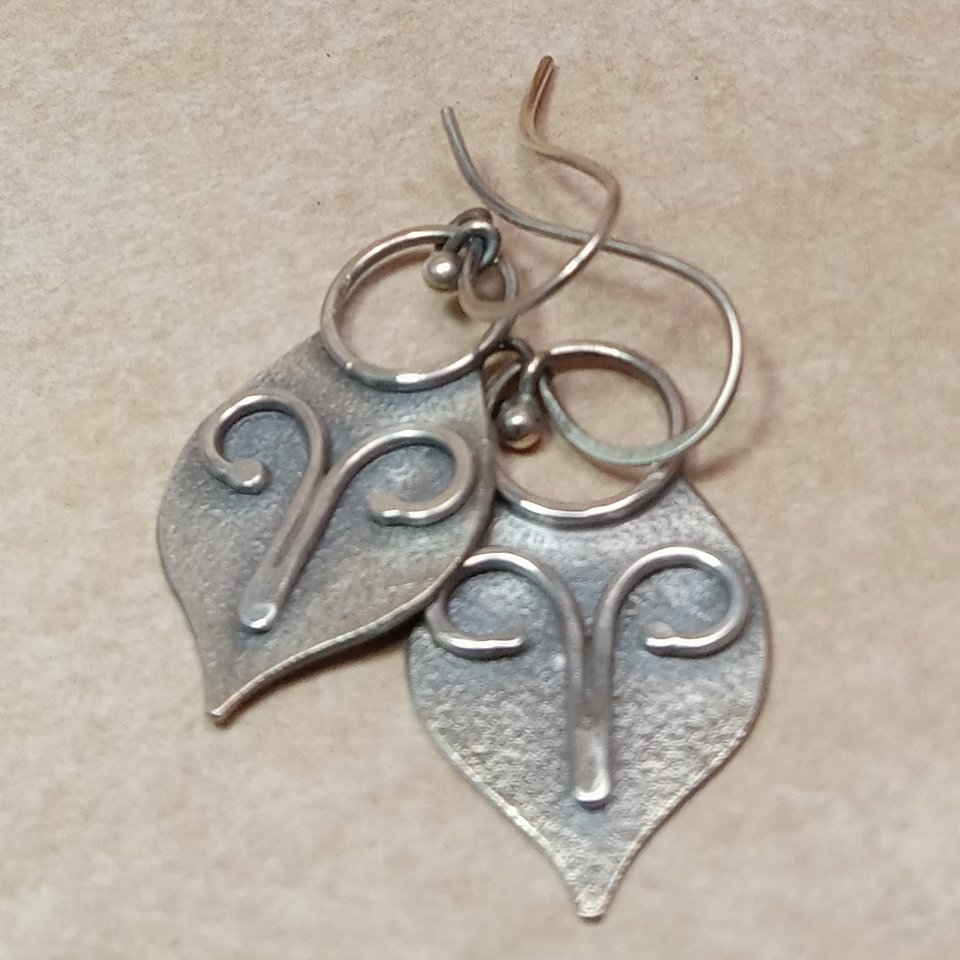 Argentium silver dangle earrings in a mask shape with wire embellishment. Displayed on neutral background.