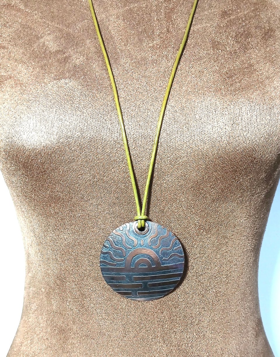 Adjustable length etched copper pendant on leather cord displayed on mannequin.