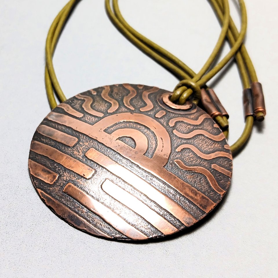 Large etched copper pendant with sun design, adjustable leather cord. Off white background.
