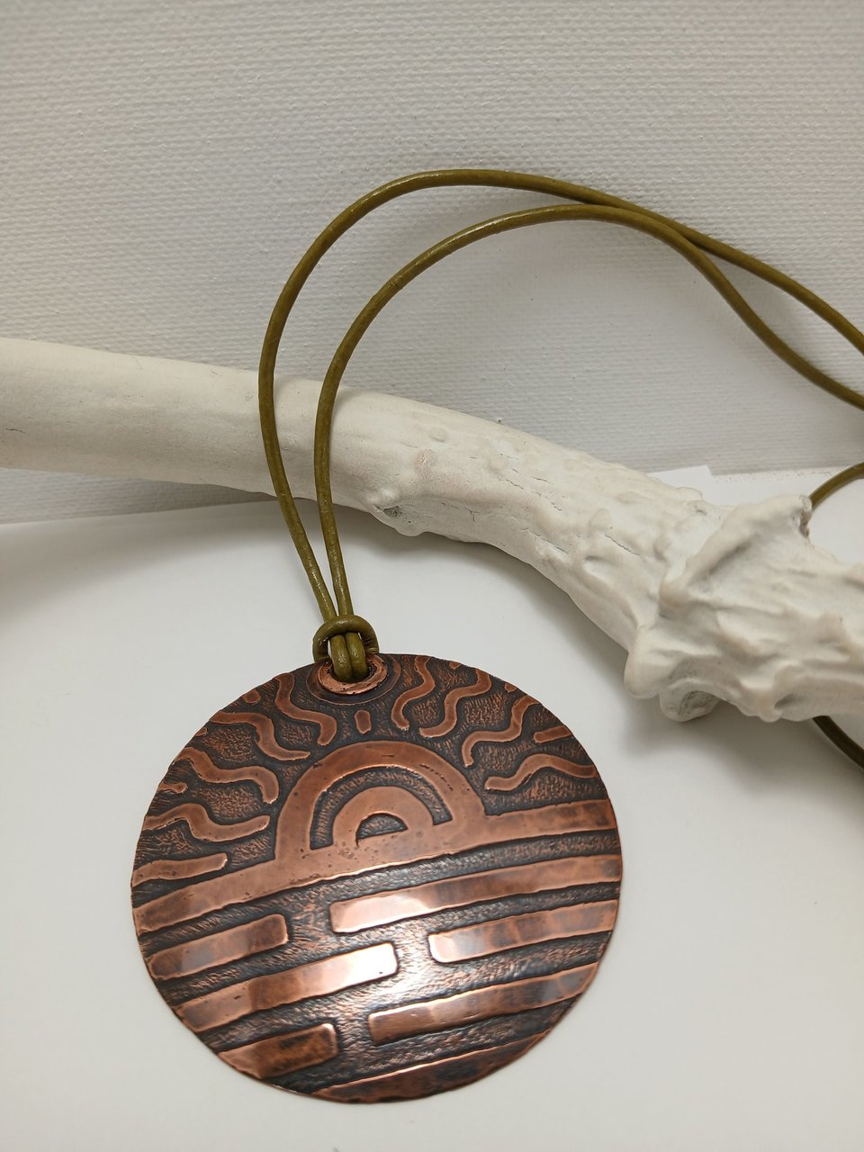 Large 2.25" copper disk pendant with etched sun design. Hung on absinthe green leather cord. Displayed against white antler on white background.