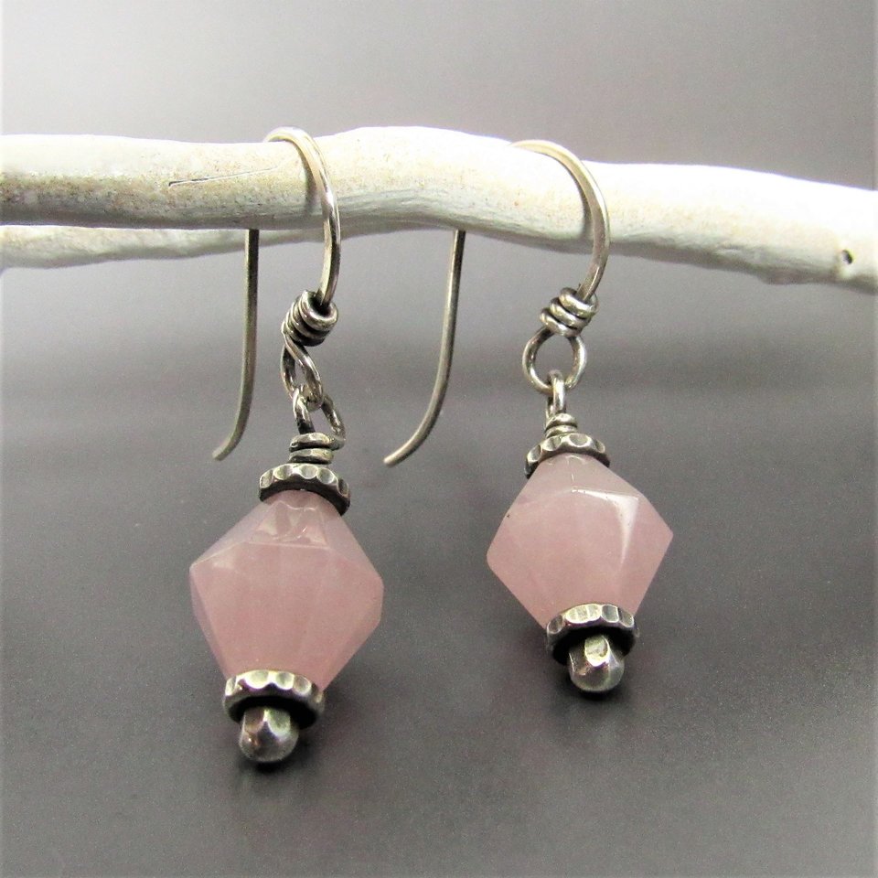 Pink quartz and sterling silver drop earrings dangling from white branch against gray background.