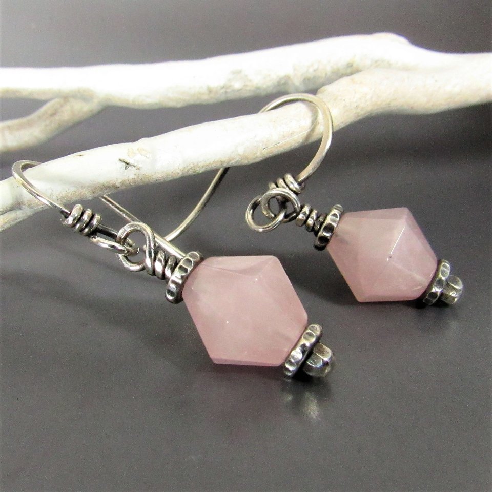 Close up of pink quartz earrings displayed against a  white branch on a gray background.
