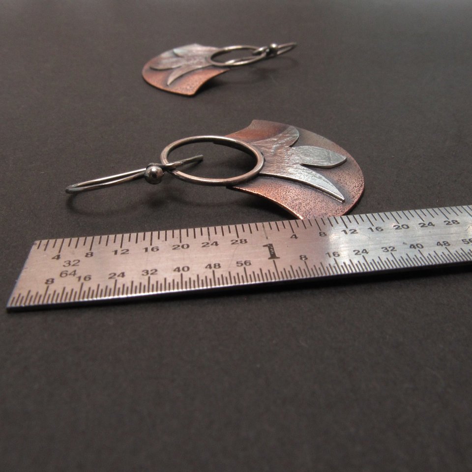Fan shape earrings in copper and silver displayed against ruler to show length. Apx. 1.5" long. Black background.