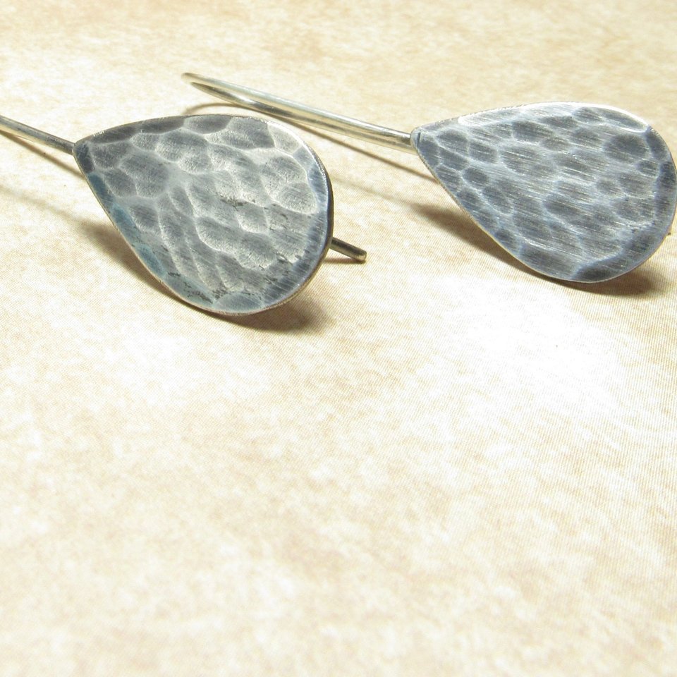 Classic tear drop earrings in hammered silver. Displayed on beige background.