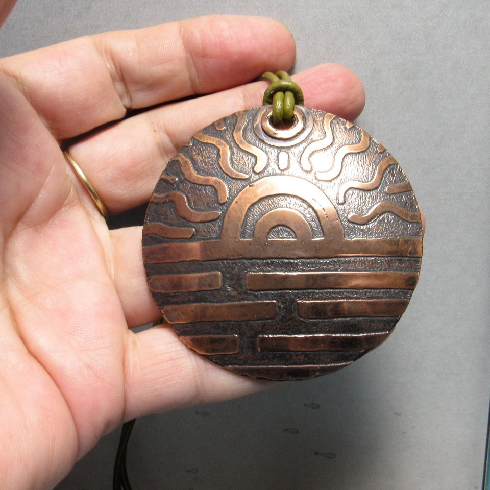 Large etched copper sun pendant displayed in hand.