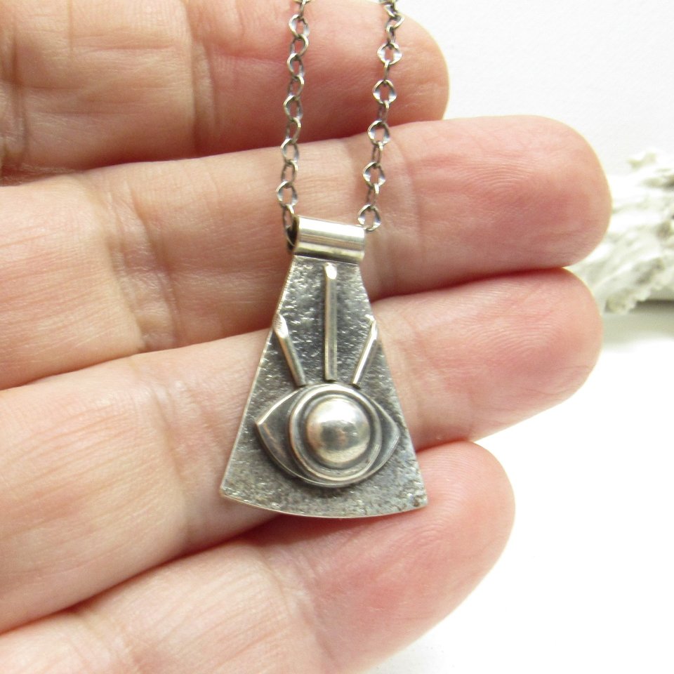 Eye of providence necklace crafted from argentium silver displayed in hand on white background.