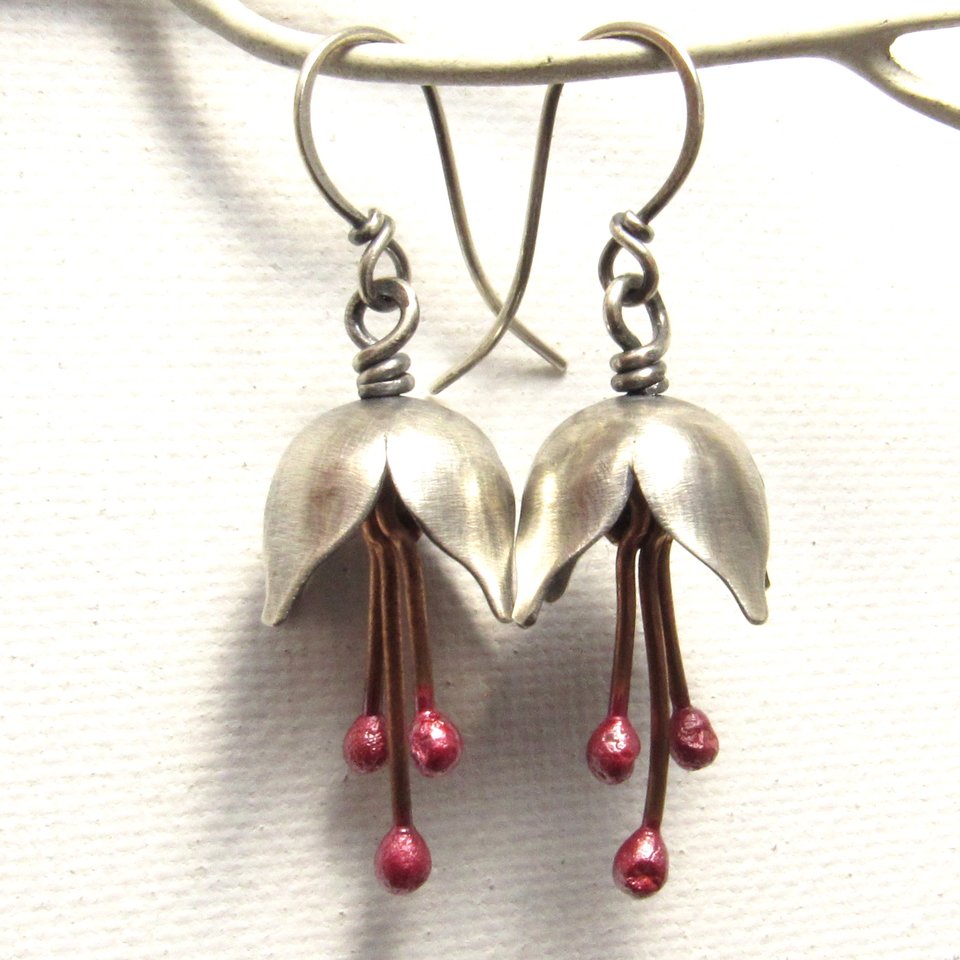 Close up of full length shot of argentium silver and pure reddened copper winter bell flower earrings. Displayed dangling from white branch on white background.
