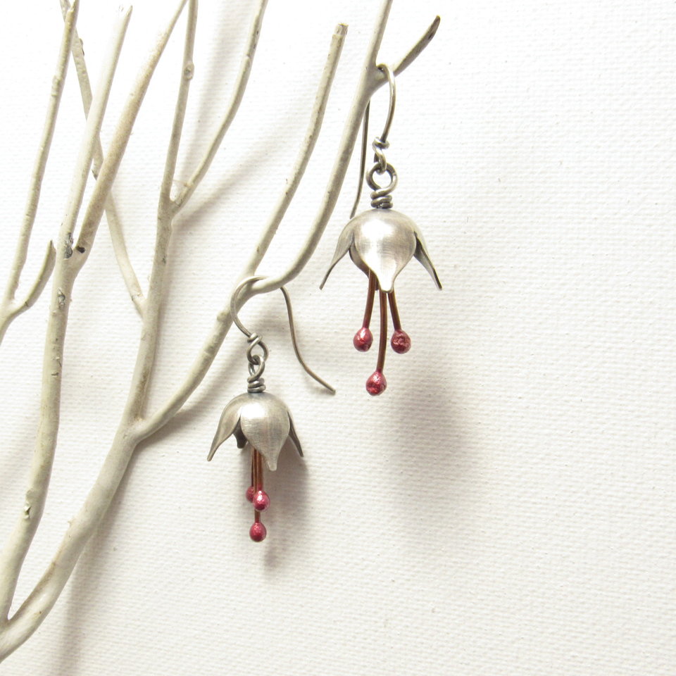 Argentium silver and pure reddened copper winter bell flower earrings. Displayed hanging one above the other on white branch on white background.