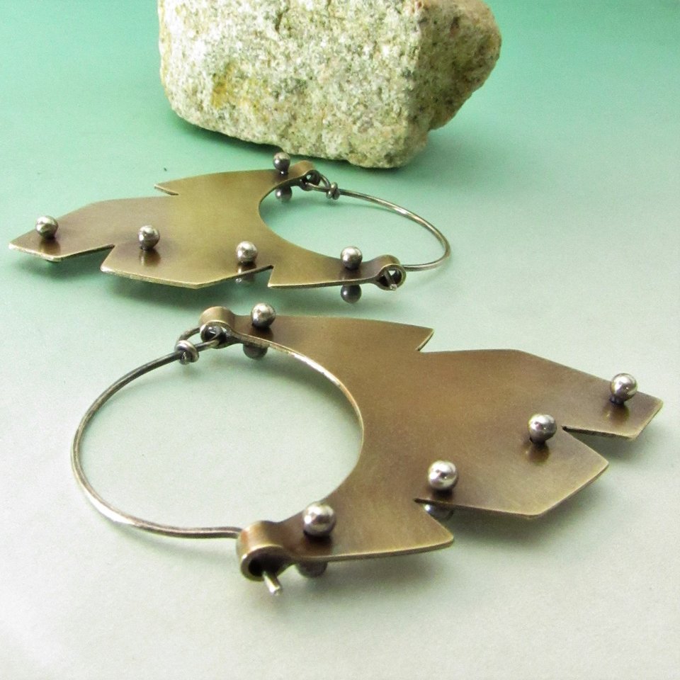 Large tribal brass hoop earrings in the shape of a stylized feather are a bold and rustic geometric design incorporating mixed metals, brass and sterling silver. 18 gauge SS ear wires. Earrings are 2.25 inch from the top of the ear wire x 1.5 wide.
