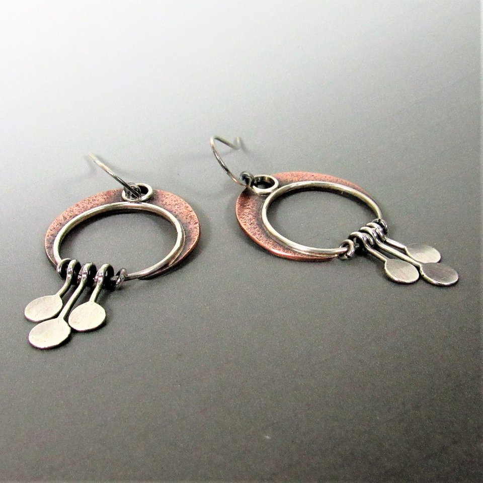 A pair of silver and copper  crescent moon earrings with a circular design and dangling silver discs. 2 inches tall and 1 " wide. Displayed on grey background.
