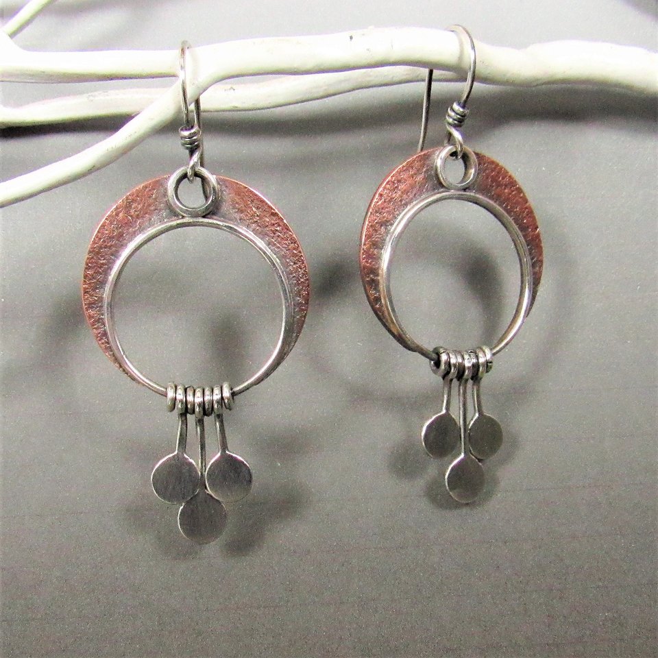 Crescent moon earrings made in copper and sterling silver with 3 silver paddles hanging beneath. Lovely movement, lightweight. 2" tall and 1" wideDisplayed on white twig against grey background.