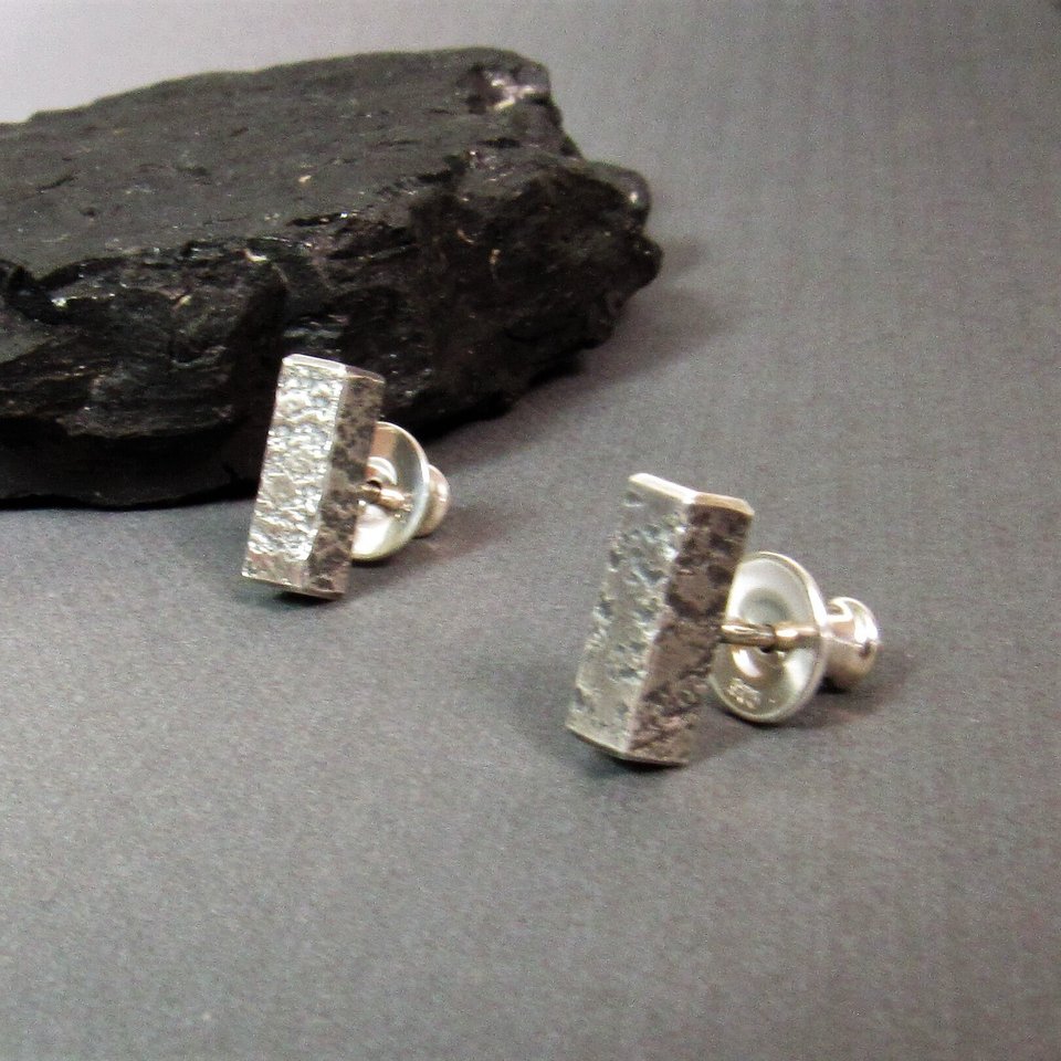 Side view of a pair of silver earrings with a textured rectangular design. The earrings are on a gray surface.