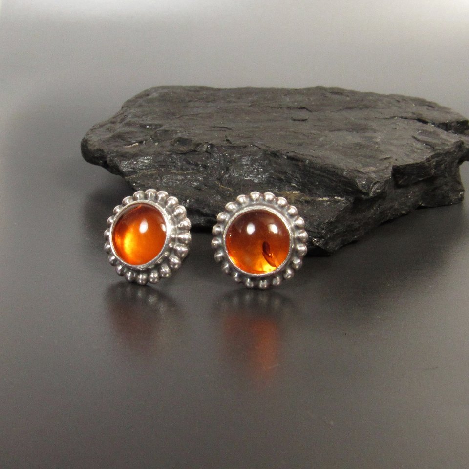 Amber and sterling silver stud earrings displayed against black rock on grey background.